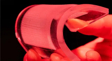 A hand bends a patch of microneedles in a red-lit image
