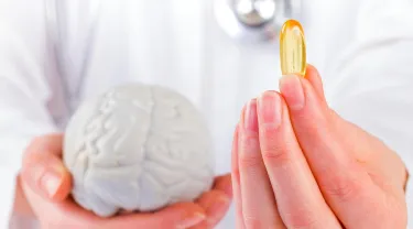 Hands holding a model of the brain and a vitamin pill