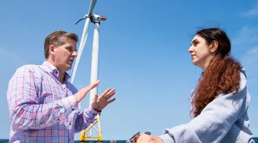 Professor Eric Hines and female student on a boat in front of Wind Turbines