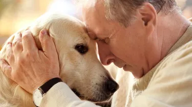 An older man in a tan sweater hugs his senior dog
