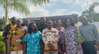 A group of people posing before an office building with palm trees to the side. Tufts researchers collaborate with two Ghanaian hospitals to break down the barriers preventing people with hypertension from getting the care they need