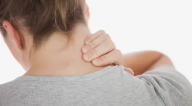 A woman seen from behind clutching her neck in pain. Tufts researchers will develop a variety of biological measures of pain, which could lead to better pain management and treatments