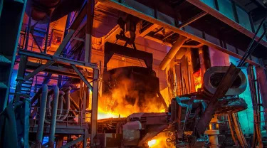 Inside a traditional steel factory, with red hot molten metal being poured. A Tufts researcher looks to use a different chemistry in ironmaking that could produce harmless water and nitrogen byproducts rather than carbon dioxide