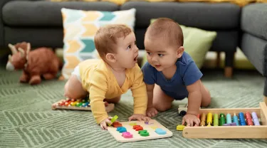 Two toddlers playing with maths toys sitting on floor at home
