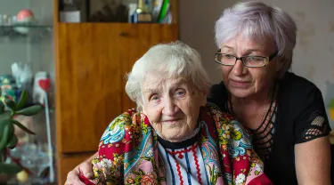 Portrait of elderly woman in bright clothes with his adult daughter sitting at home