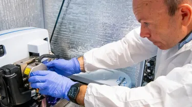 A photo of a researcher in a white coat and purple gloves working with lab equipment