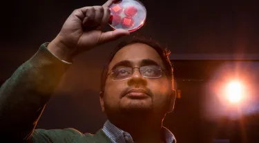 A man wearing glasses examines a transparent disk with red circles inside it that he holds above his head 