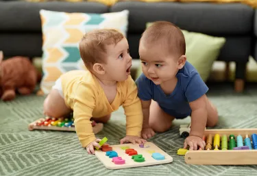 Two toddlers playing with maths toys sitting on floor at home