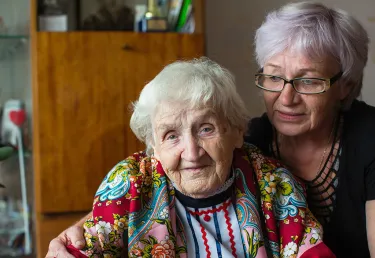 Portrait of elderly woman in bright clothes with his adult daughter sitting at home