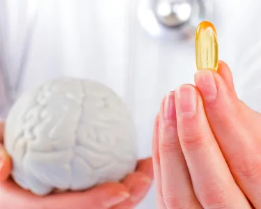 Hands holding a model of the brain and a vitamin pill