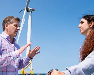 Professor Eric Hines and female student on a boat in front of Wind Turbines