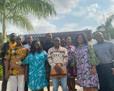 A group of people posing before an office building with palm trees to the side. Tufts researchers collaborate with two Ghanaian hospitals to break down the barriers preventing people with hypertension from getting the care they need
