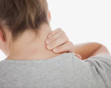 A woman seen from behind clutching her neck in pain. Tufts researchers will develop a variety of biological measures of pain, which could lead to better pain management and treatments