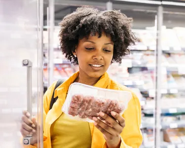 Woman in yellow sweater choosing package of ground meat in supermarket