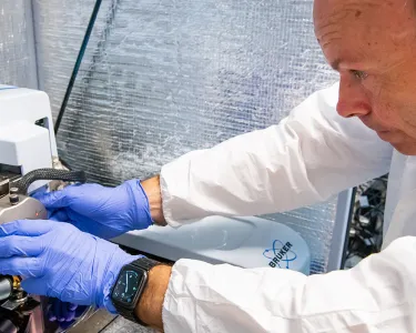 A photo of a researcher in a white coat and purple gloves working with lab equipment