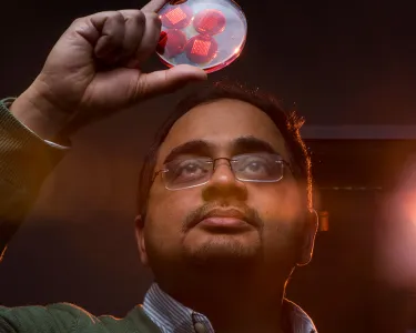 A man wearing glasses examines a transparent disk with red circles inside it that he holds above his head 